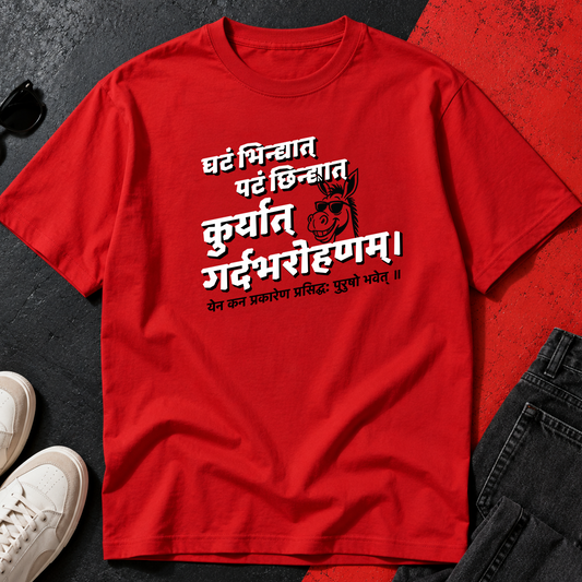  red short-sleeve T-shirt laid flat on a dark textured surface, with white Sanskrit
 text and a cartoon graphic printed on the front. White sneakers and dark jeans are placed around it as styling props.