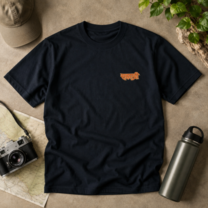 A navy blue short-sleeve t-shirt with a large graphic print of a hiking backpack featuring a mountain, waterfall, and the Hindi word 'Sahyadri' in orange. 
