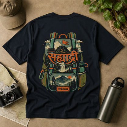 A navy blue short-sleeve t-shirt with a large graphic print of a hiking backpack featuring a mountain, waterfall, and the Hindi word 'Sahyadri' in orange. 