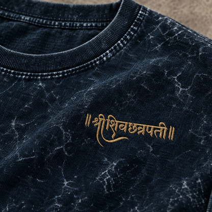 Close-up of a dark navy acid-wash t-shirt featuring gold embroidered Devanagari script on the chest.