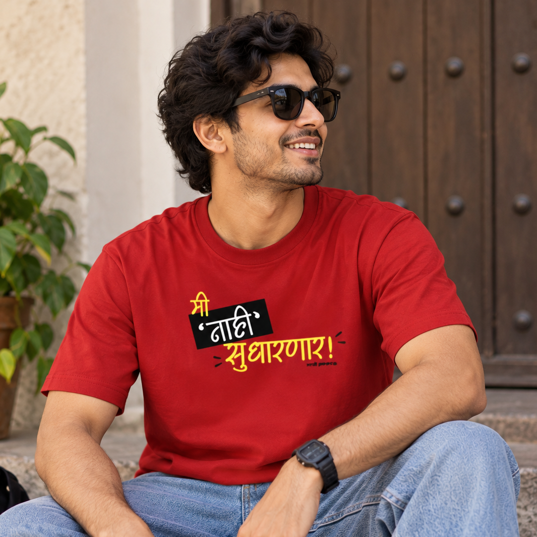 A man wearing a bright red graphic t-shirt and blue jeans sits on stone steps outdoors. The t-shirt features a bold black and yellow Marathi slogan.